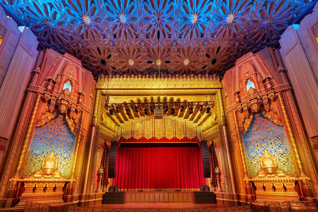 Theater with ornate red stage and colorful ceiling.