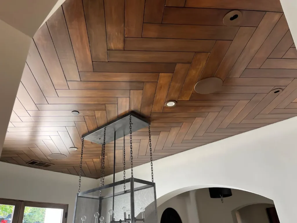 Herringbone-patterned wooden ceiling with lighting fixture.