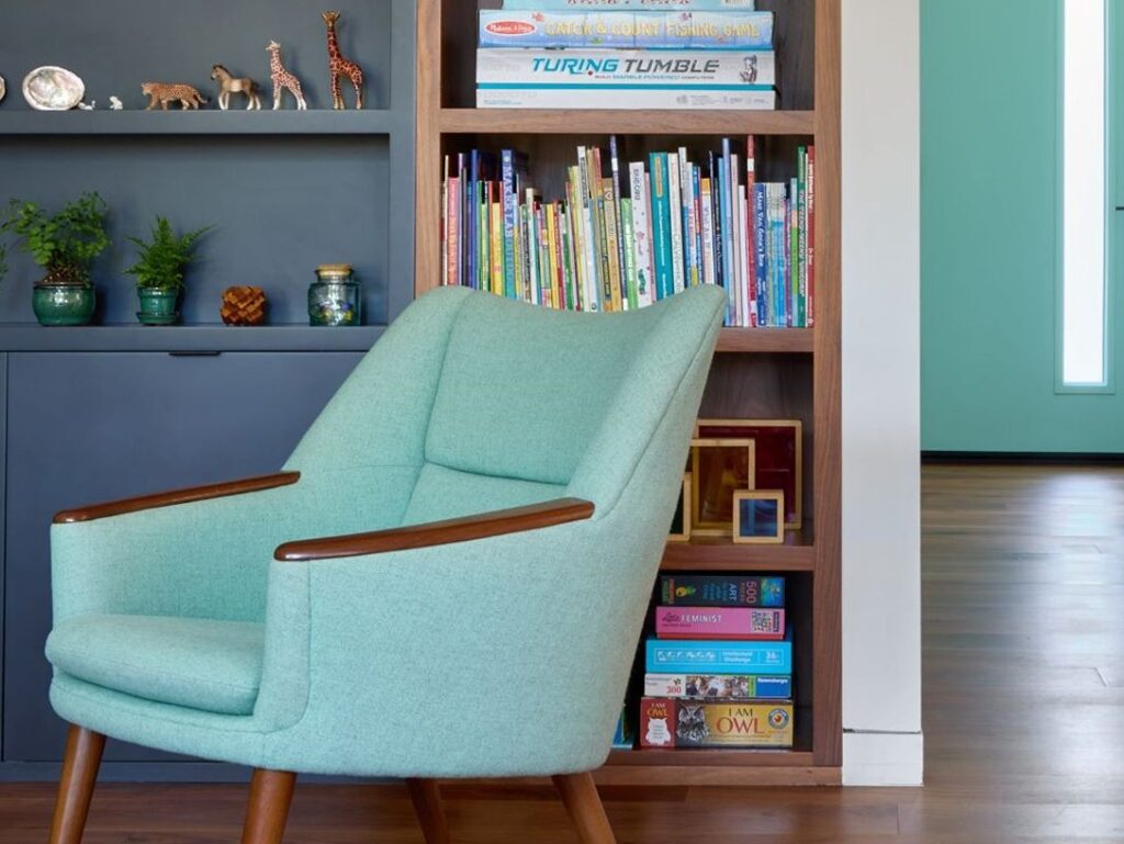 Teal armchair near colorful bookcase shelf